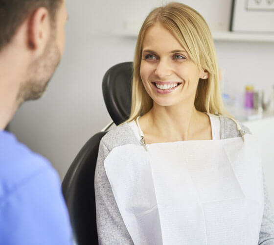 Smiling woman patient in dental chair consulting with dentist about gum tissue regeneration.
