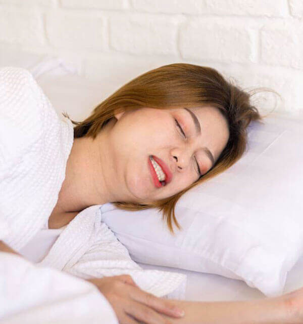 Woman sleeping peacefully on white pillow, representing relief from teeth grinding and clenching.