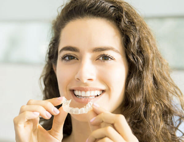 Woman inserting clear Invisalign aligner to straighten teeth and improve her smile.