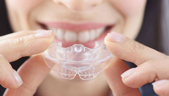 Woman holding a clear dental night guard while smiling at the camera.