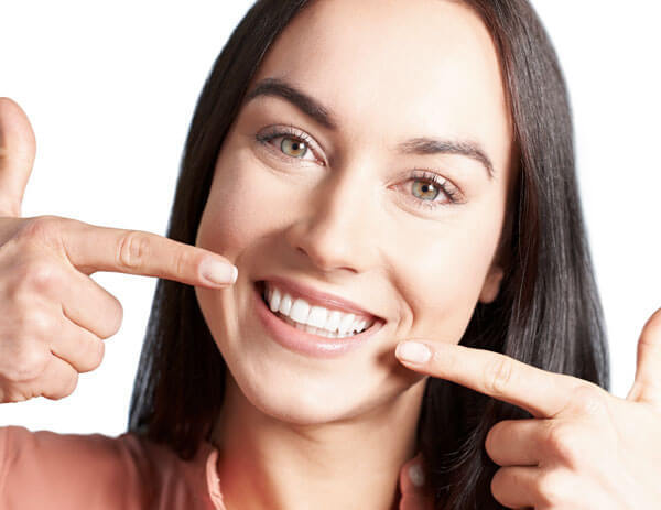 Woman pointing to her bright white smile and teeth, demonstrating dental results.