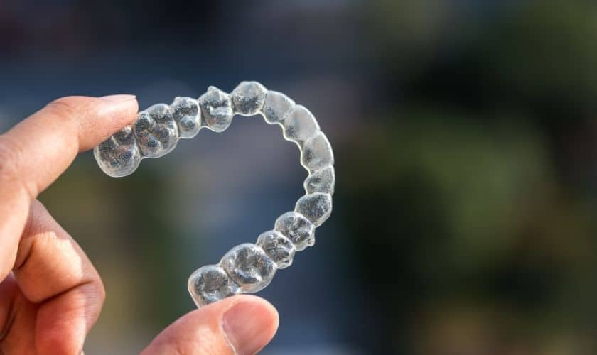Clear aligner tray held in hand showing the sequential stages of invisible orthodontic treatment.
