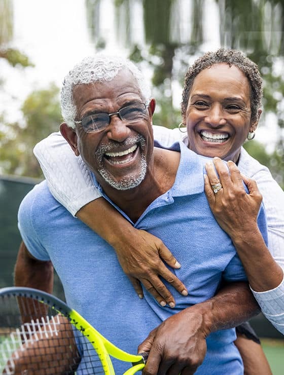 Two men smiling together outdoors with a tennis racket, representing healthy, confident smiles.