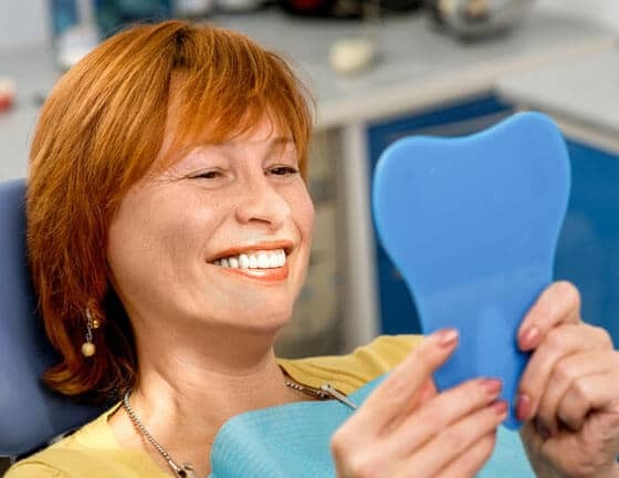 Happy patient holding blue heart shape in dental office.