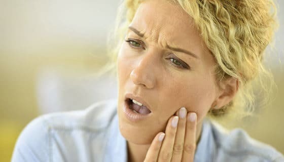 Woman experiencing dental pain, holding her cheek in discomfort during a dental emergency.