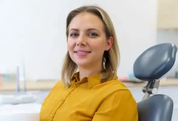Woman in yellow shirt smiling in dental office treatment room.